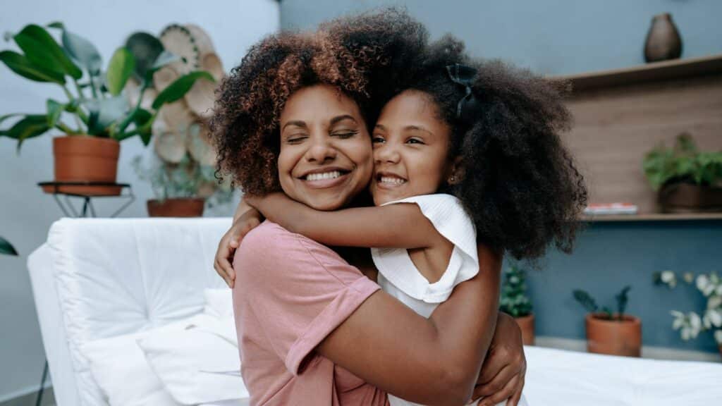 Mãe e filha se abraçando enquanto as duas sorriem, durante a comemoração do Dia das Mães.