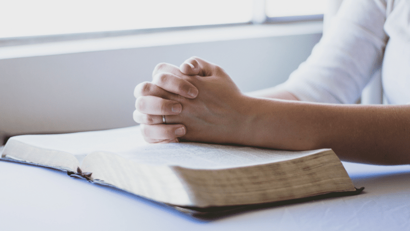 Mãos de mulher sobre a bíblia, juntas, rezando.