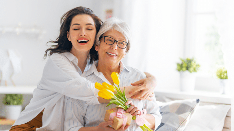 Filha abraçando a mãe enquanto segura uma flor