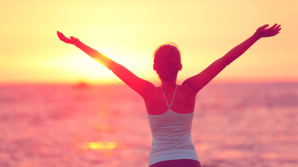 Conceito de bem-estar, de viver bem a vida e felicidade. Silhueta de mulher com braços abertos levantados para o céu em uma praia praticando Yoga.