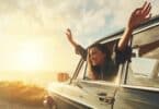 Imagem de um pôr do sol em uma praia. Em destaque um carro e uma mulher toda feliz, abrindo os braços na janela do carro mostrando que está vivendo a vida intensamente.