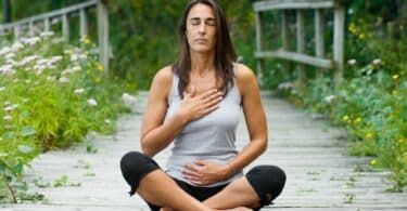 Mulher meditando em volta de jardim.