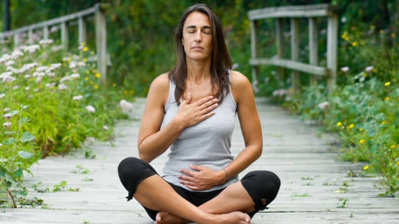 Mulher meditando em volta de jardim.