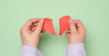 Duas mãos femininas rasgando um coração de papel vermelho, simbolizando uma decepção.