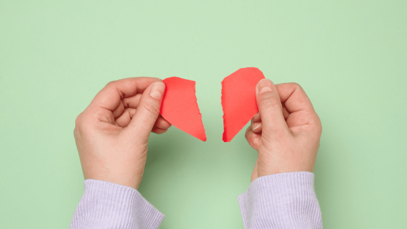 Duas mãos femininas rasgando um coração de papel vermelho, simbolizando uma decepção.