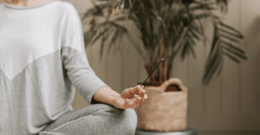 Mulher sentada, meditando em sua casa, enquanto segura um incenso.