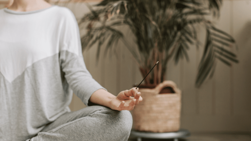 Mulher sentada, meditando em sua casa, enquanto segura um incenso.