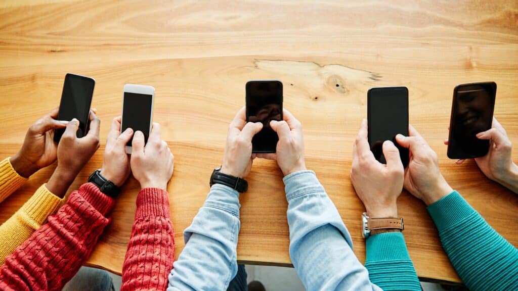 Grupo de pessoas, sentadas em uma mesa, usando seus celulares. 