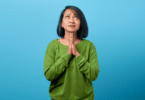 Mulher asiática com as mãos juntas, em sinal de perdão.