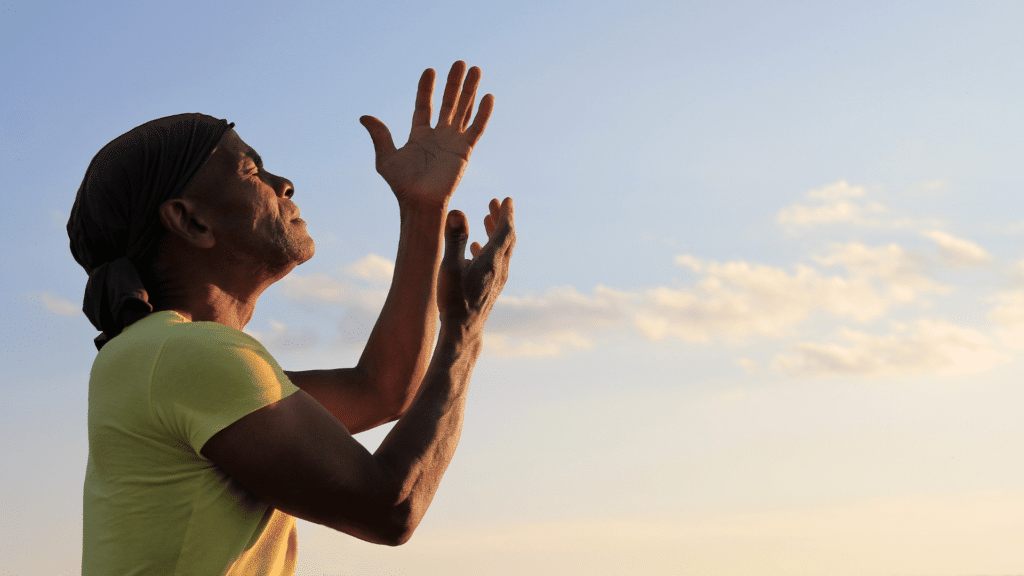 Homem com as mãos para o alto, rezando e clamando por Deus, em fundo com céu azul. 