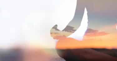 Pessoa sentada em posição de Yoga, em areia de praia.
