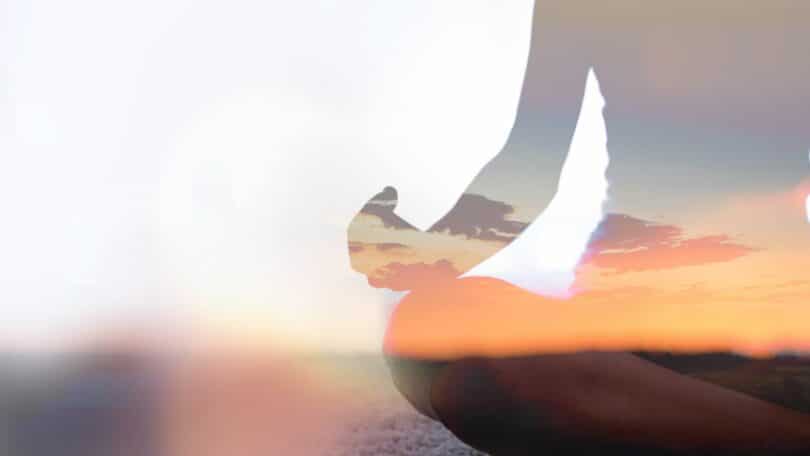 Pessoa sentada em posição de Yoga, em areia de praia.