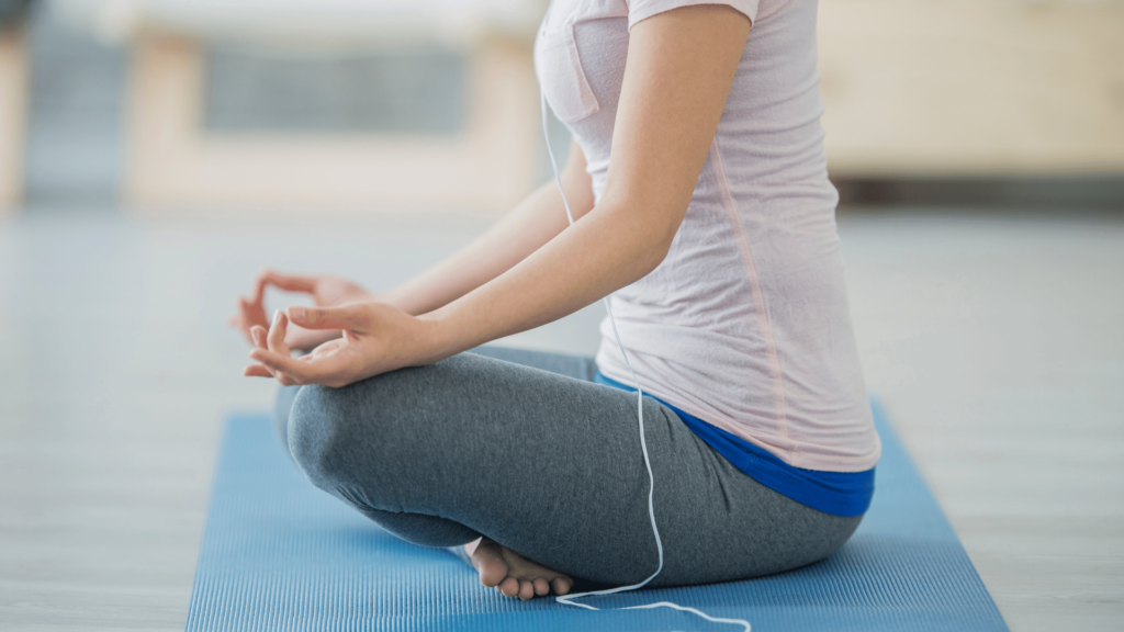 Pessoa sentada em posição de Yoga, escutando música por fone de fio. 