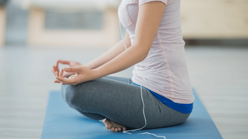 Pessoa sentada em posição de Yoga, escutando música por fone de fio.