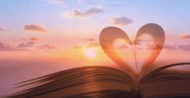 Imagem de um céu com o Sol ao fundo. Em destaque a imagem de um livro e um coração, representando a leitura, sabedoria e conhecimento