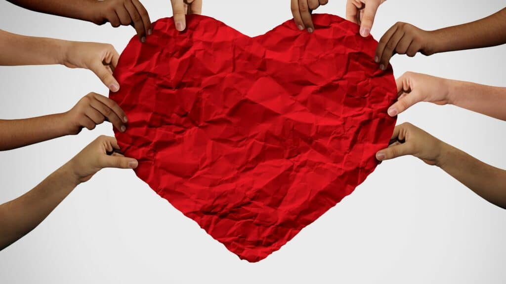 Imagem de várias mãos segurando um enorme coração feito de papel.