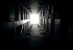 Imagem de um corredor escuro e no fim dele uma porta com uma luz ao fundo.