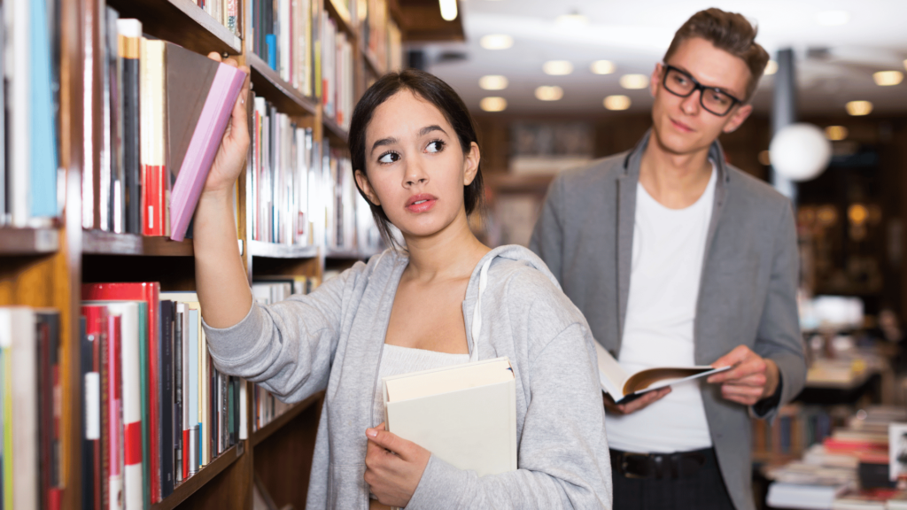 Menina escolhendo livros atrai atenção de um homem. 