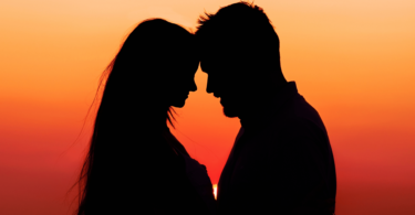 Sombra de casal com as faces encostadas, em fundo laranja de pôr do sol.