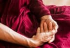Imagem de um monge budista usando uma roupa vermelha. Ele está sentado, praticando a meditação.