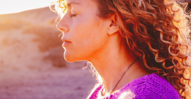 Retrato de uma mulher com os olhos fechados, sentindo o pôr do sol em sua face.