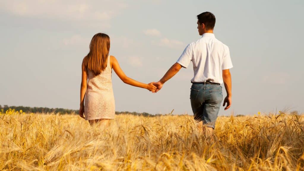 Imagem de um casal de mãos dadas, caminhando em um campo de trigo.