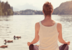 Mulher meditando em frente de lago.