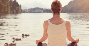 Mulher meditando em frente de lago.
