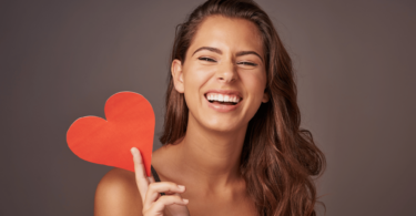 Mulher sorrindo enquanto segura coração vermelho de papel.