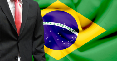 Homem vestido de terno. Ao funo, a bandeira do Brasil. Conceito de candidato político.