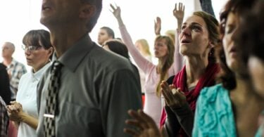 Imagen de várias pessoas, homens e mulheres, louvando a Deus dentro de uma igreja.