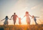 Imagem de uma família feliz, composta pelos pais e os três filhos, caminhando de mãos dadas sob o pôr do Sol.