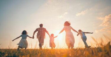 Imagem de uma família feliz, composta pelos pais e os três filhos, caminhando de mãos dadas sob o pôr do Sol.