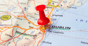 Há um grande pin vermelho no centro da imagem e colocado sobre a cidade de Dublin (na Irlanda) em um mapa-múndi.