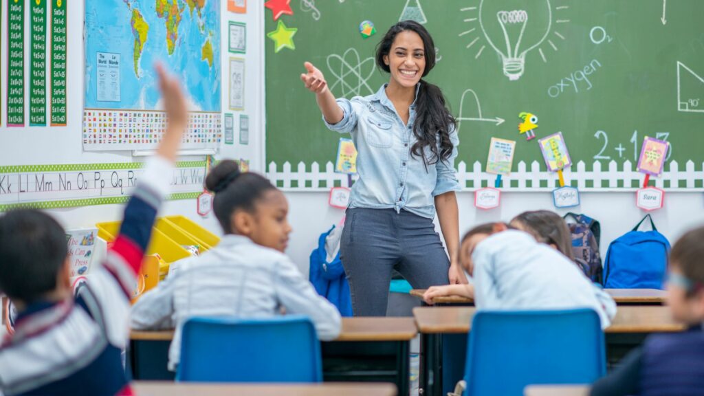 Imagem de uma professora em sala de aula junto com os seus alunos.
