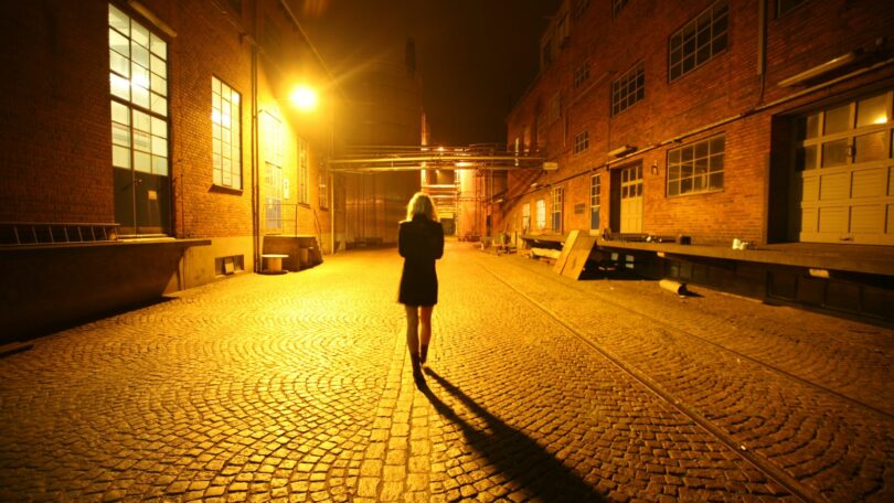 Imagem de fundo amarelo de uma mulher andando na rua sozinha durante a noite.