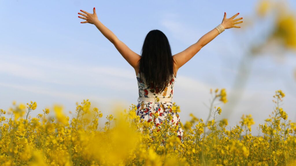Imagem de uma mulher de cabelos longos e pretos, de costas e de braços abertos para o céu, transmitindo a sensação de liberdade.
