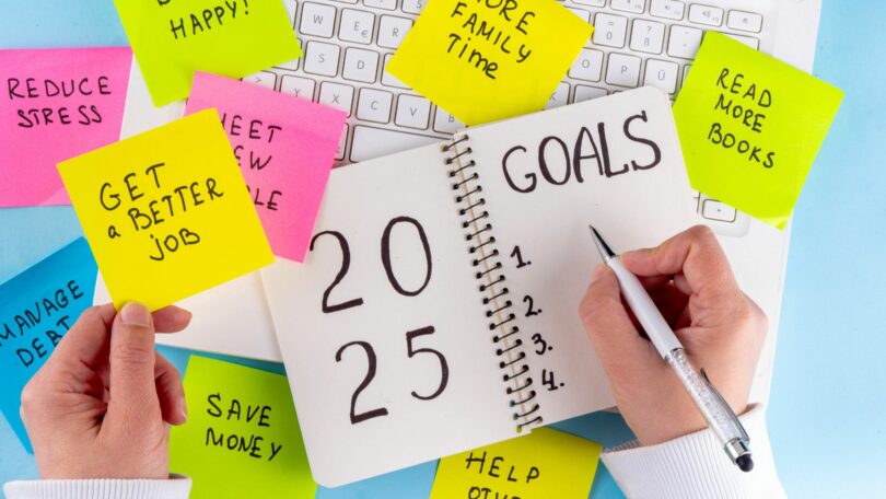 Imagem de um notebook e sobre ela um caderno e vários post-its coloridos com frases e palavras de motivações para o novo ano de 2025.