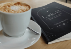 Uma xícara de café e um livro intitulado "Lado B" estão em cima de um banco e no centro da imagem.