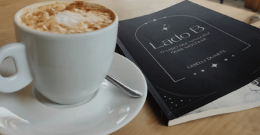Uma xícara de café e um livro intitulado "Lado B" estão em cima de um banco e no centro da imagem.