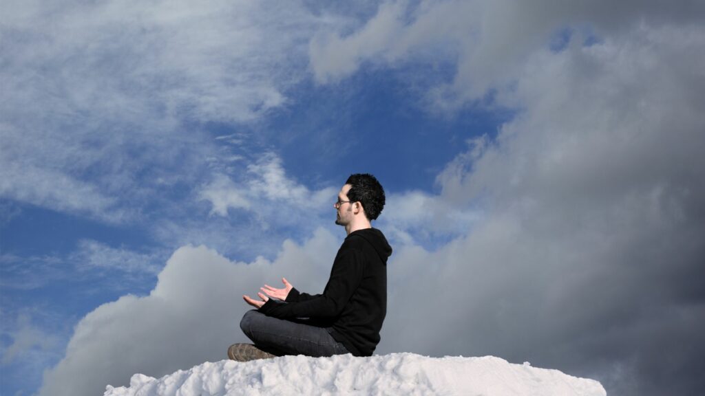 Imagem de um homem e,m posição de meditação, sentando sobre um chão coberto com neve, trazendo o conceito sobre o sentido da vida.
