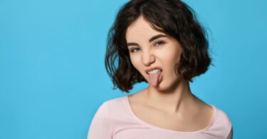 Imagem de fundo azul e em destaque uma jovem mulher mostrando a língua, trazendo o conceito de menosprezo.
