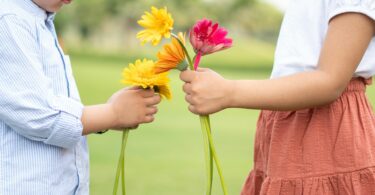 Imagem de uma pequena garota entregando flores a um pequeno jovem, simbolizado a gratidão, o carinho, a doação de coisas boas.
