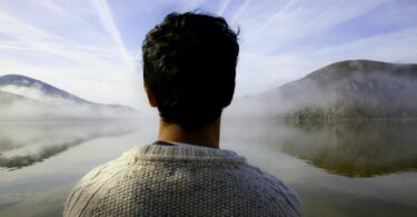 Imagem de um lago e em volta dele, duas montanhas. Em destaque, um homem, olhando para o futuro, trazendo o conceito de valorização da vida.