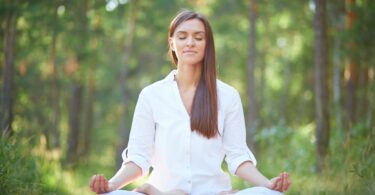 Imagem de uma mulher usando roupa branca. Ela está sentando em posição de yoga praticando a meditação e fazendo o hoponopono.