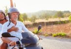 Imagem de um casal maduro passeando de moto em uma estrada cheia de montanhas e áreas verdes.