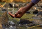 Imagem de uma fonte de água natural e limpa e a mão de uma pessoa tocando nesta água.