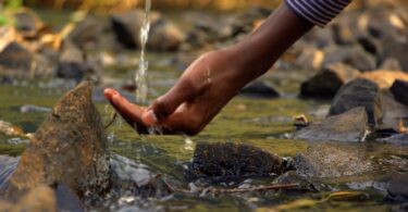 Imagem de uma fonte de água natural e limpa e a mão de uma pessoa tocando nesta água.