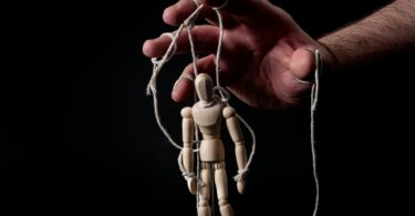Imagem de uma mão masculina manipulando um modelo de brinquedo de madeira.