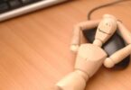 Imagem de um boneco de madeira deitado sobre um mouse, de barriga para cima em uma mesa de computador, trazendo o conceito de pausa das redes digitais.